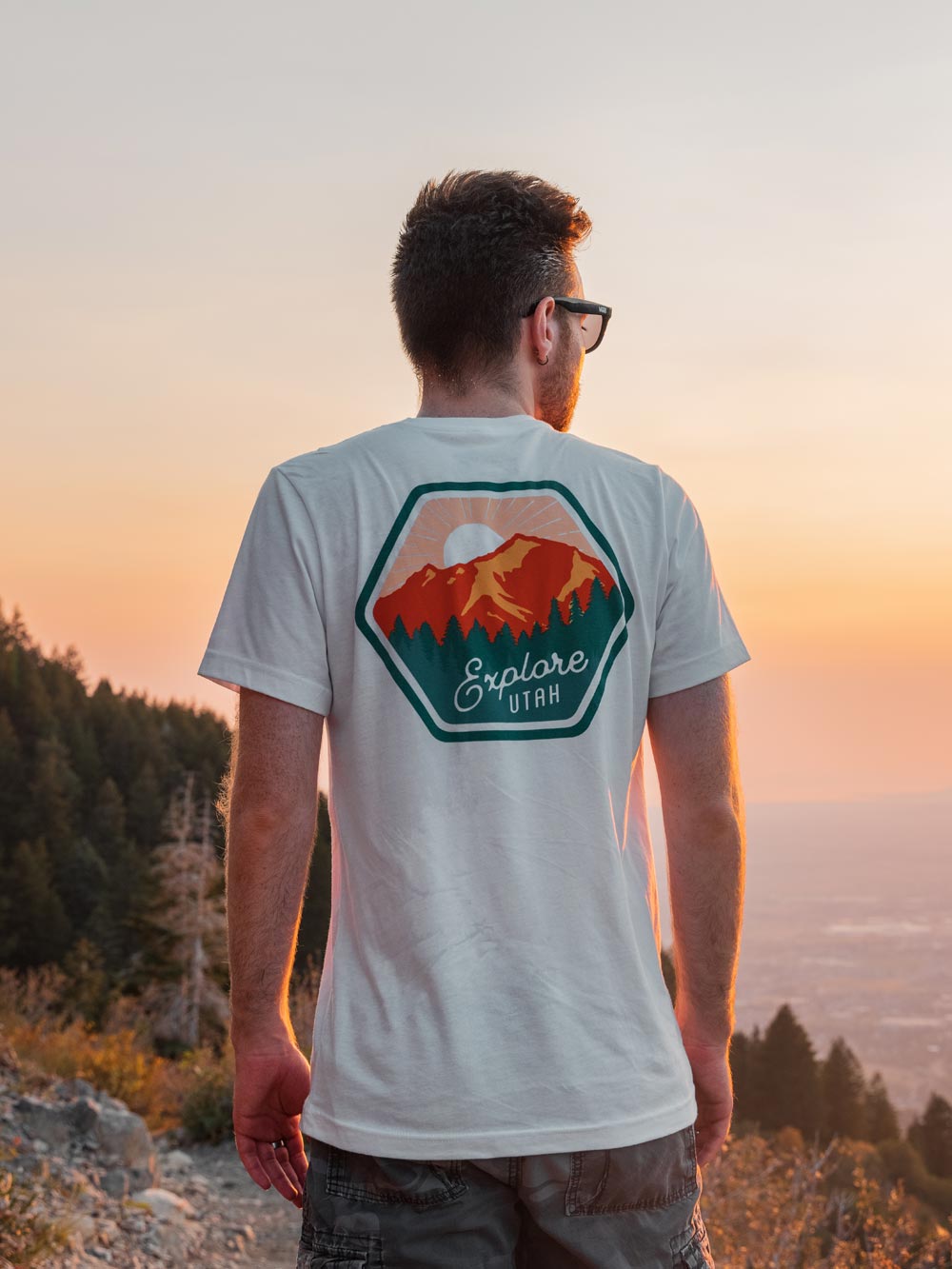 El Manor Ave Co-Founder Chase Charaba facing away from the camera and toward the sunset while showing off the white Explore Utah t-shirt.